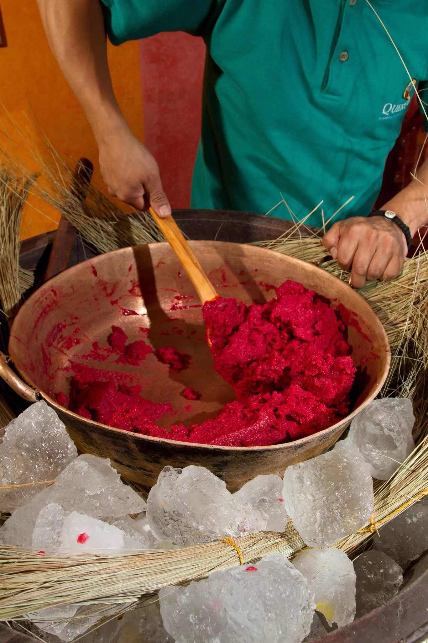 A person stirs dark pink ice cream in a bronze pot over ice in Ecuador