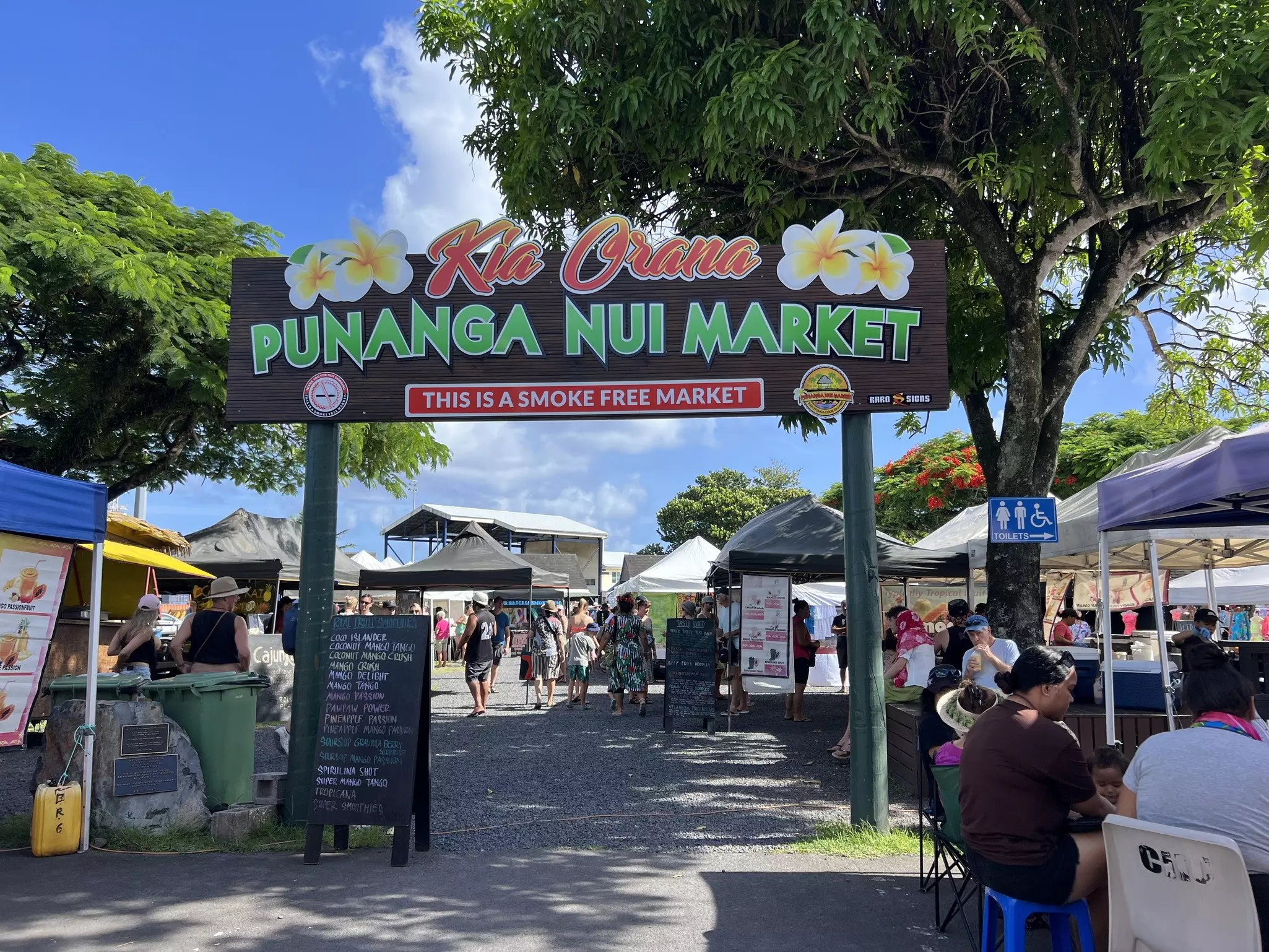 A large wooden sign marks the entrance to Punanga Nui Market with stalls of food vendors, crafts and live cultural and music performances.