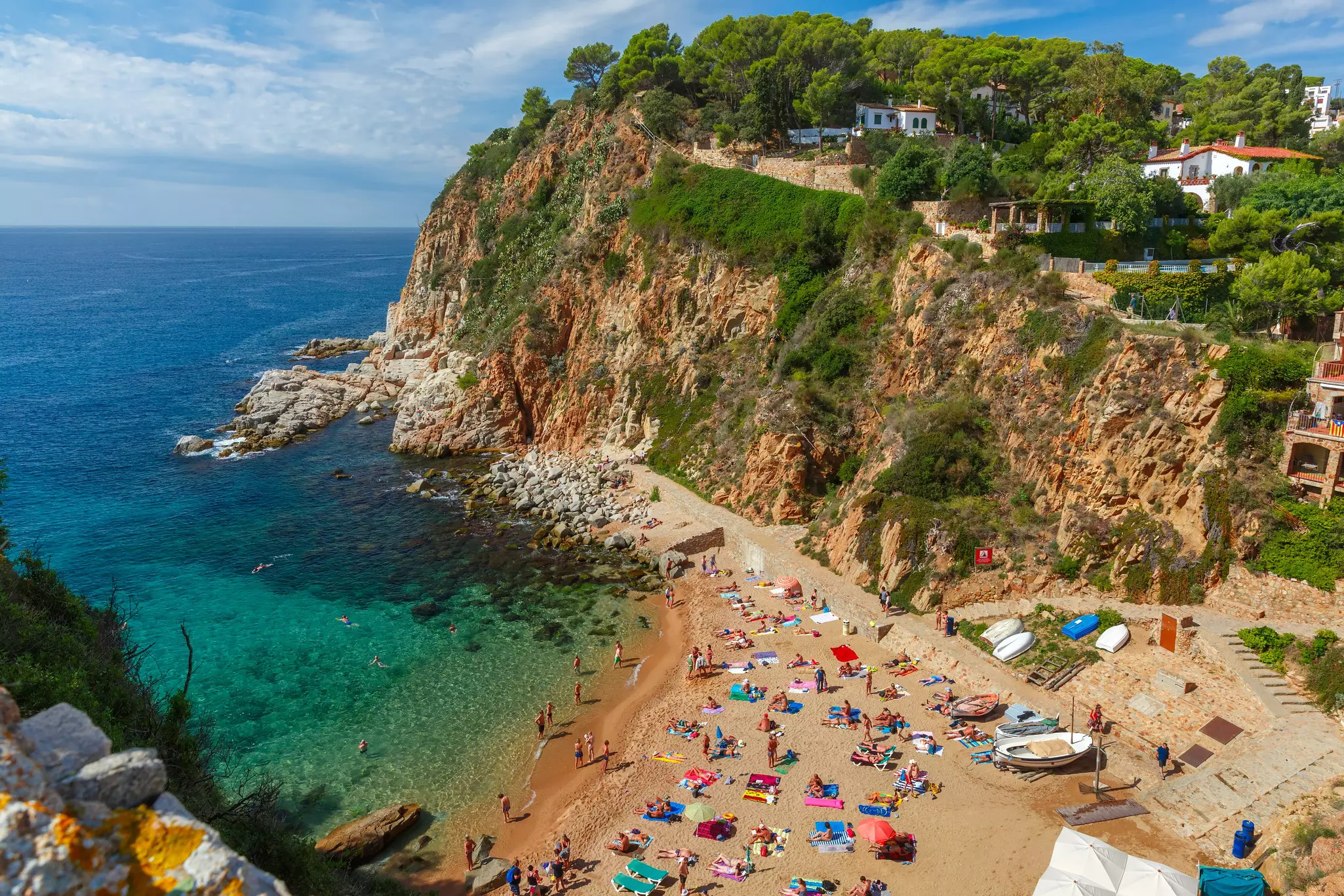 A beach with cliffs on one side. People are lying on beach towels in the sunshine.