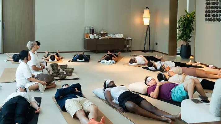 People wearing sleep masks lie in a circle with their heads pointing toward the center.