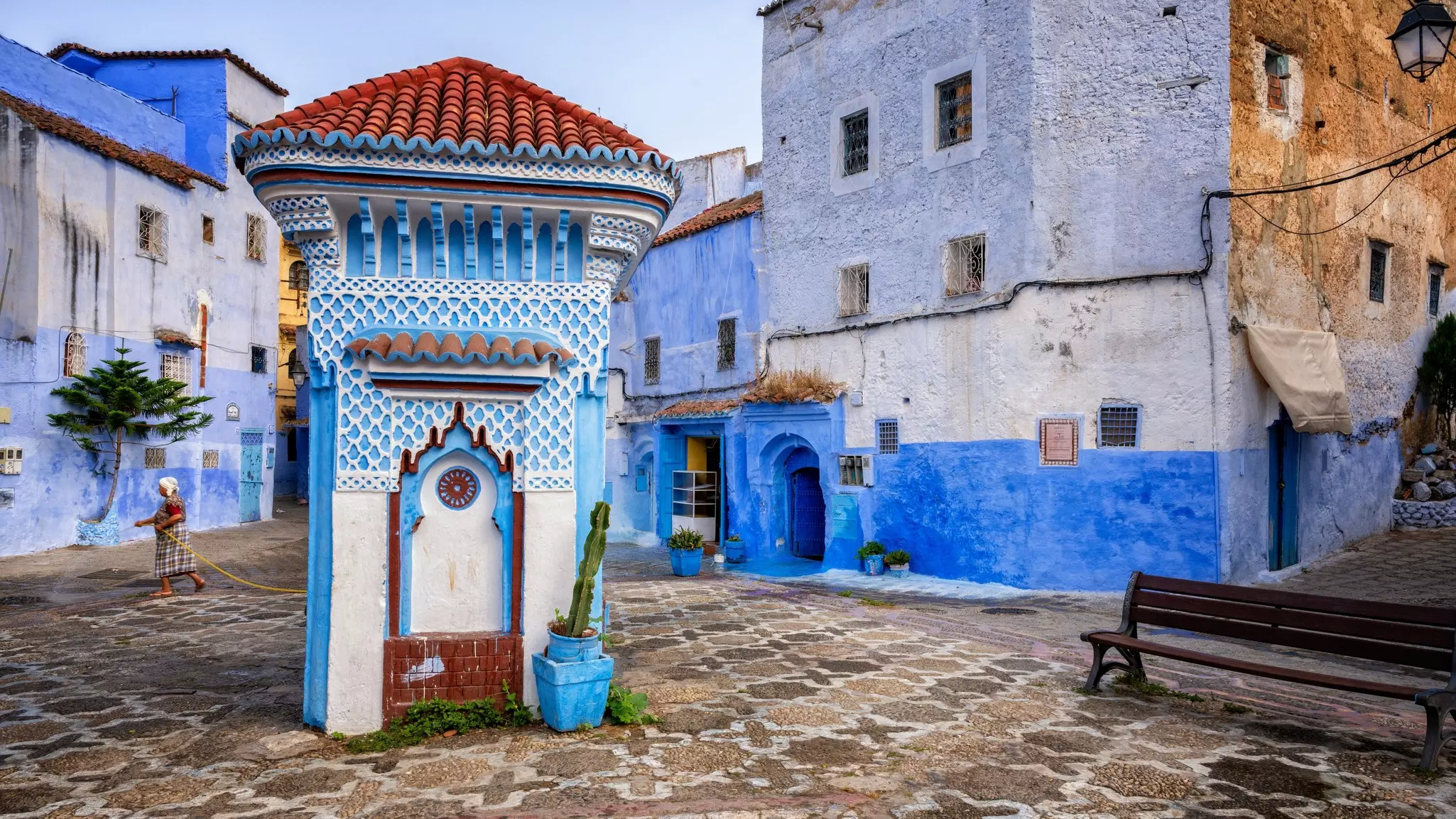 A decorated blue-and-white water fountain in a square in Morocco; the surrounding buildings are washed in shades of blue.