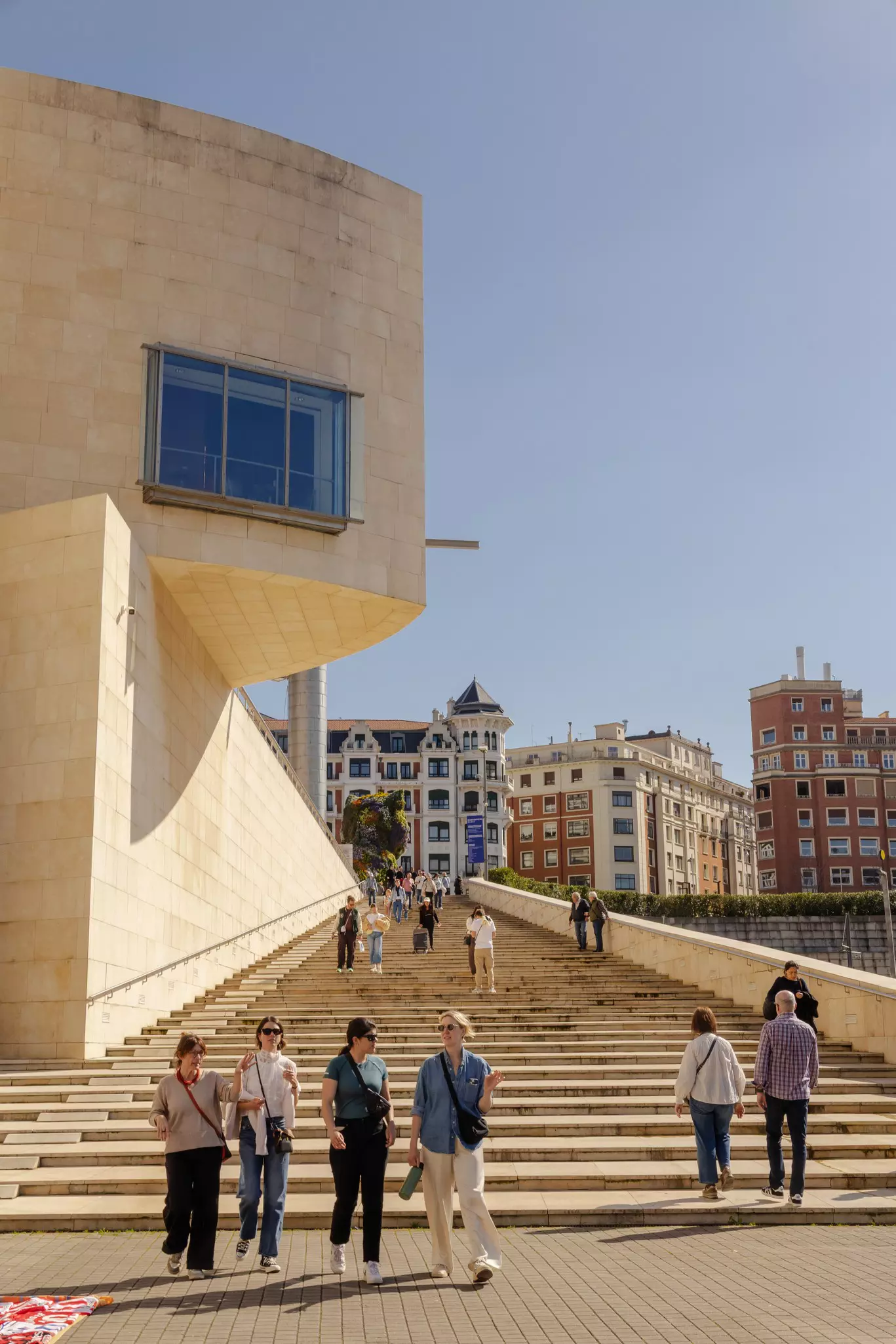 A small group of four women walk down stairs in a city on a sunny day.