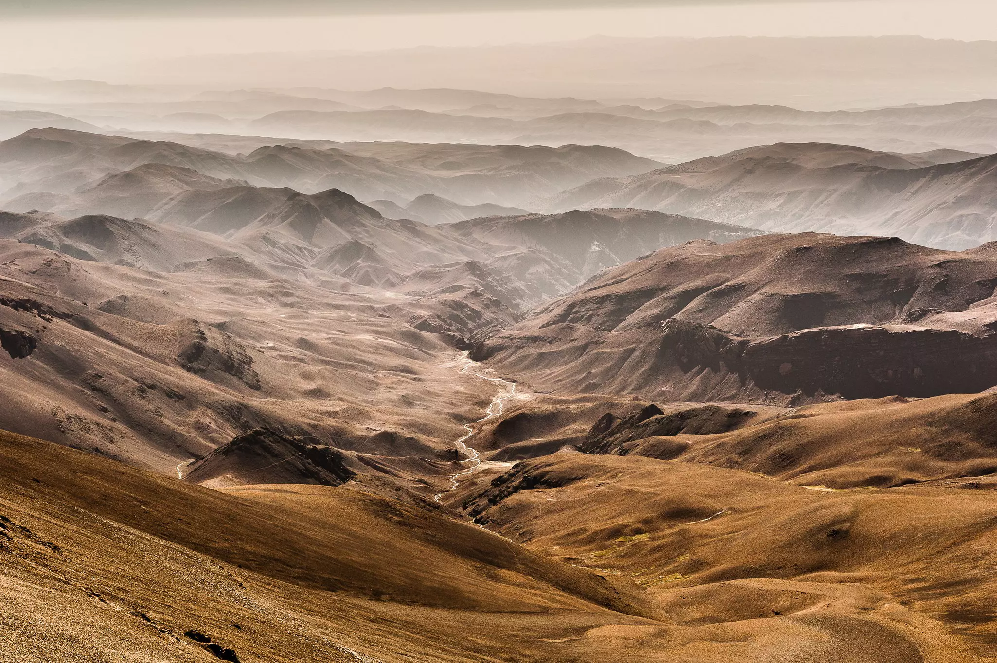 A view down over the desert-like foothills of the High Atlas Mountains; streams meander and low mist hangs in the lower valleys.