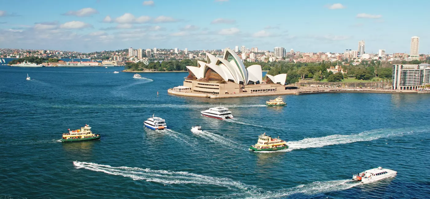 The Sydney Opera House, with several boats around it in the blue harbor.