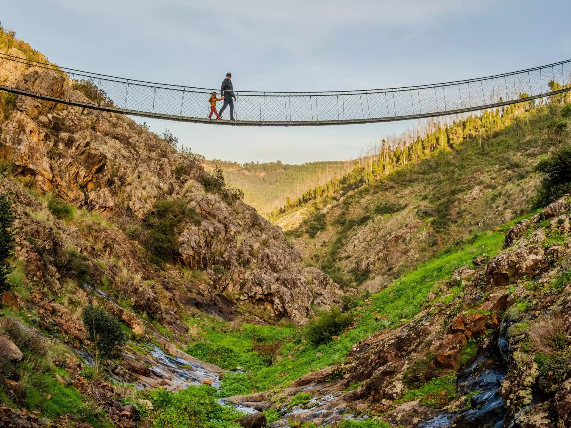 A father and son walk across a hanging bridge in the village of Alferce in Portugal.