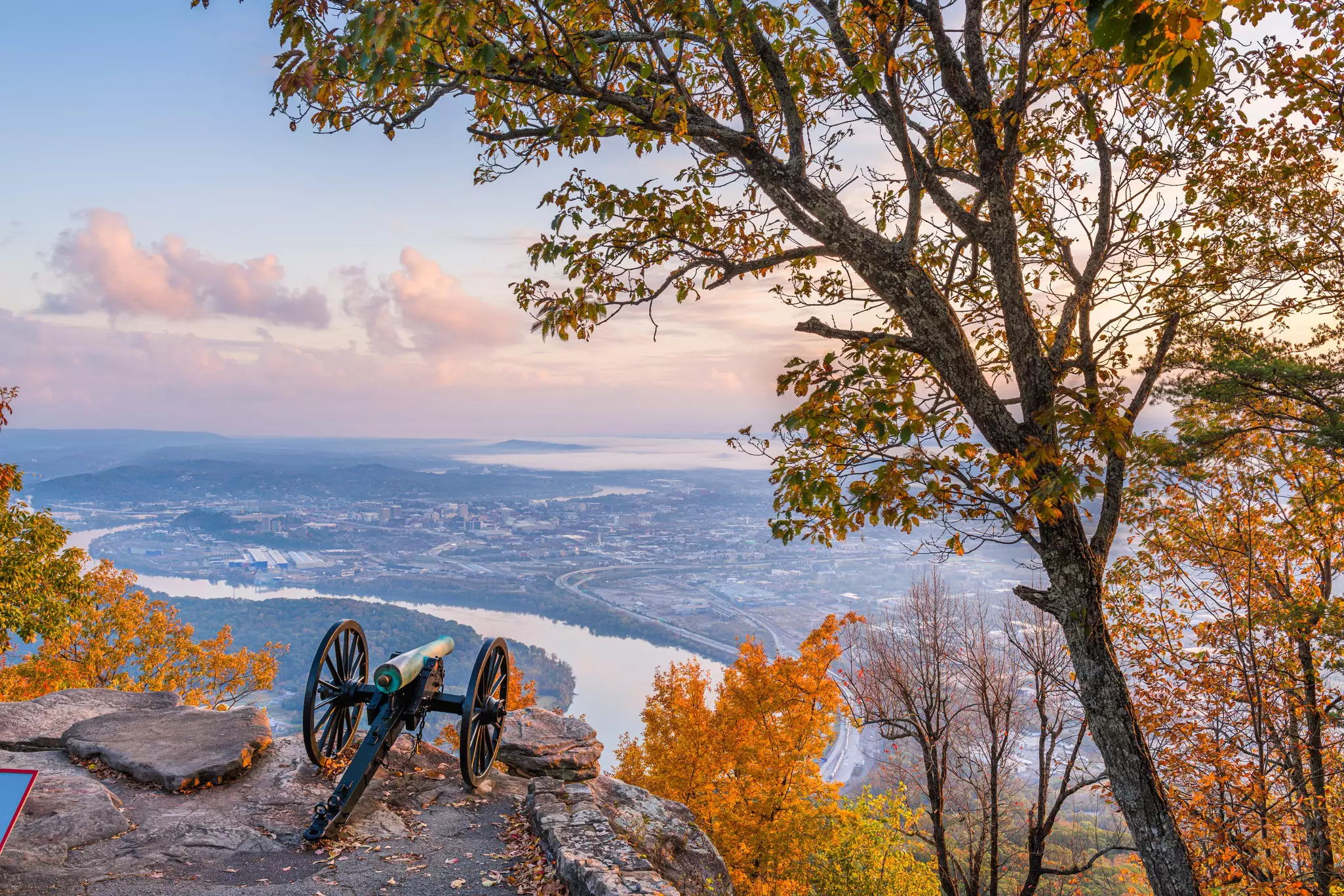 A canon mounted on wheels at the edge of a viewpoint down to a riverside city