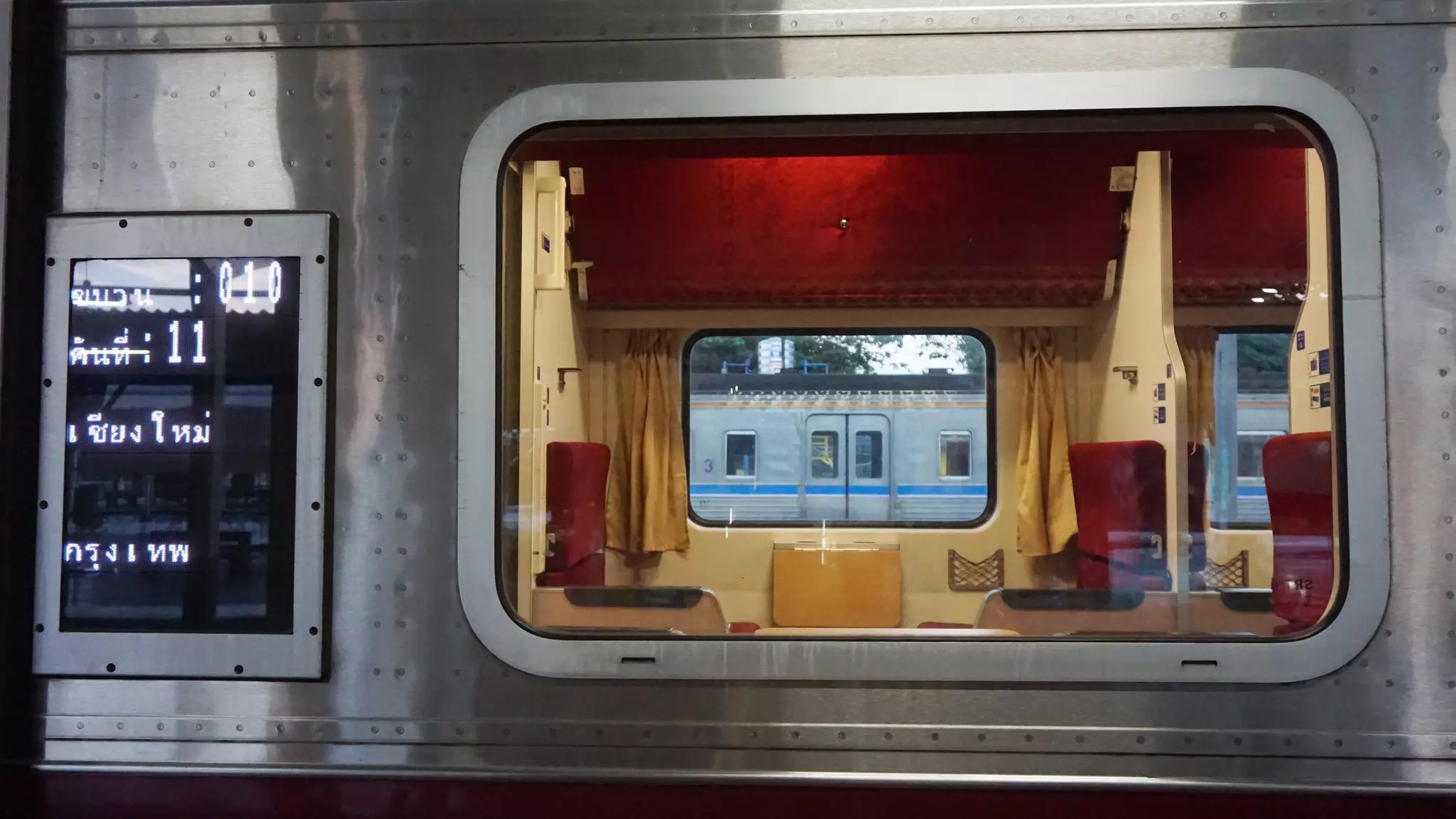The exterior of a train car showing sleeper compartments through a large window is pictured in a station.