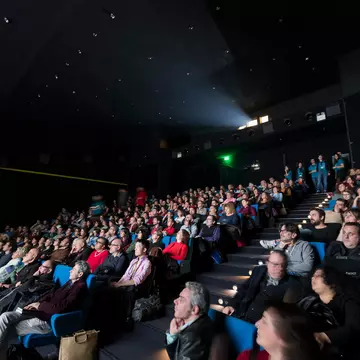 People seated in a raked cinema watch a film screening.