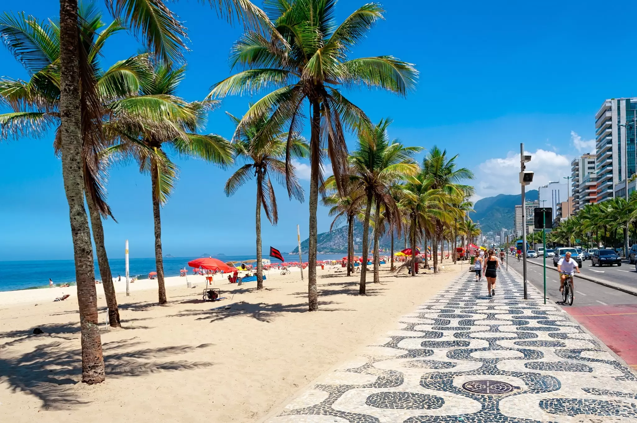 People walking along the mosaic sidewalk by Ipanema Beach lined with palm trees in Rio de Janeiro, Brazil.