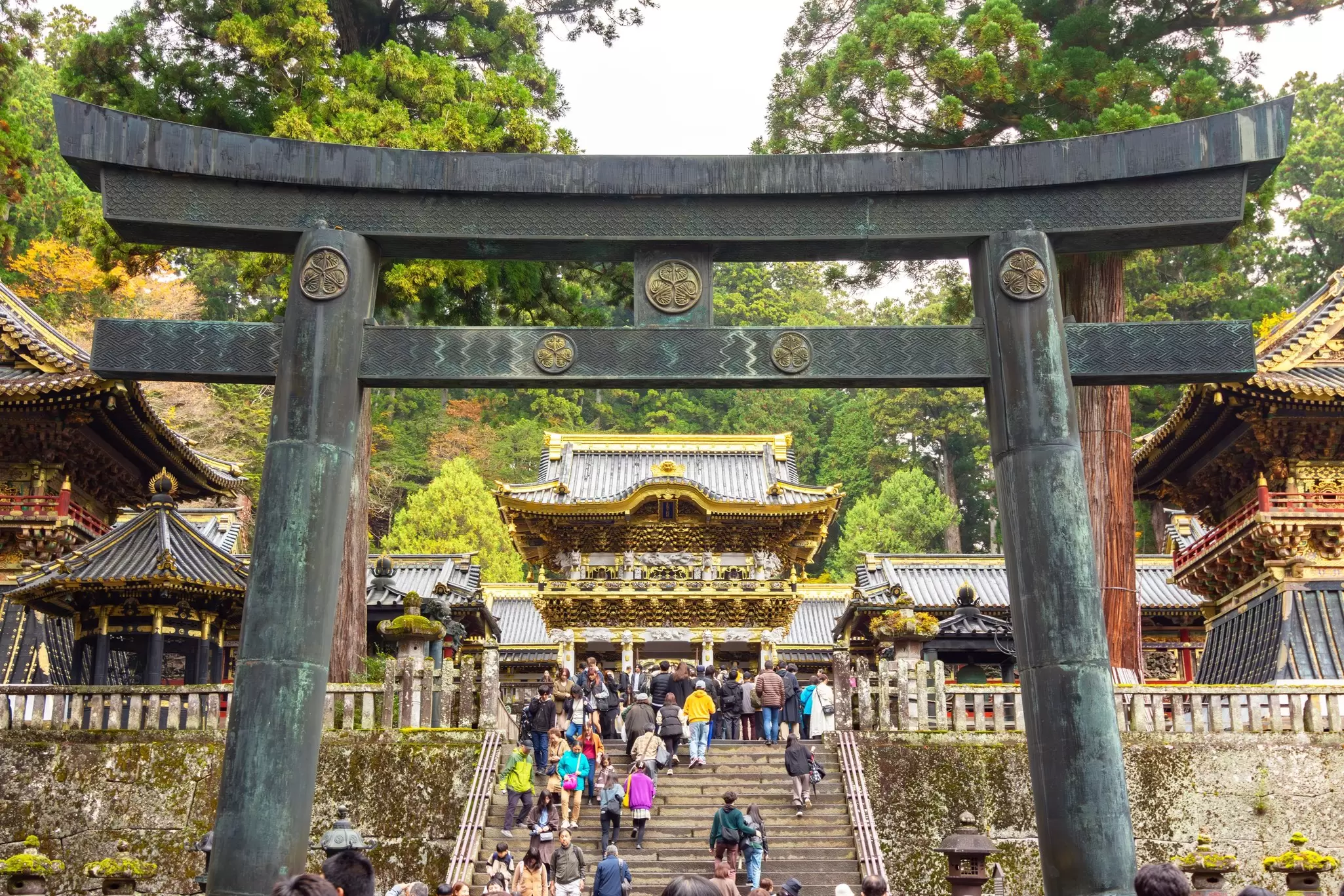 People climb steps under a stone gate leading to a temple complex.