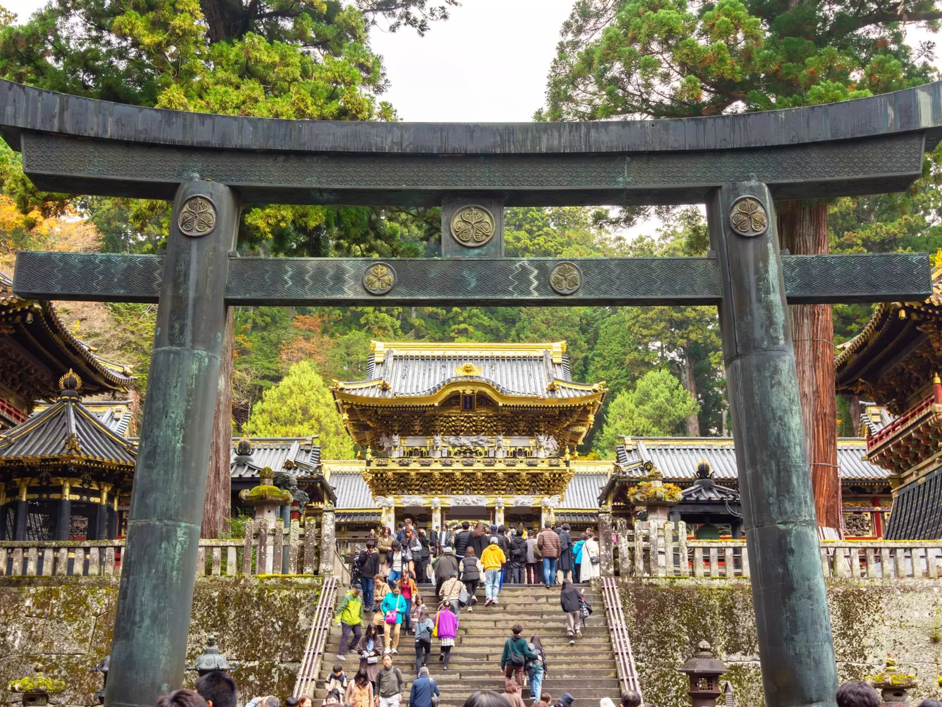 People climb steps under a stone gate leading to a temple complex.
