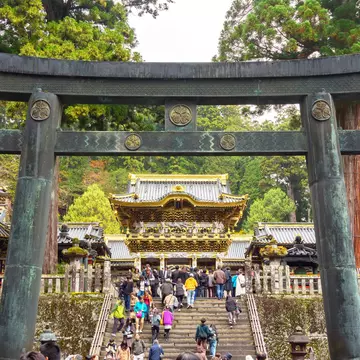People climb steps under a stone gate leading to a temple complex.