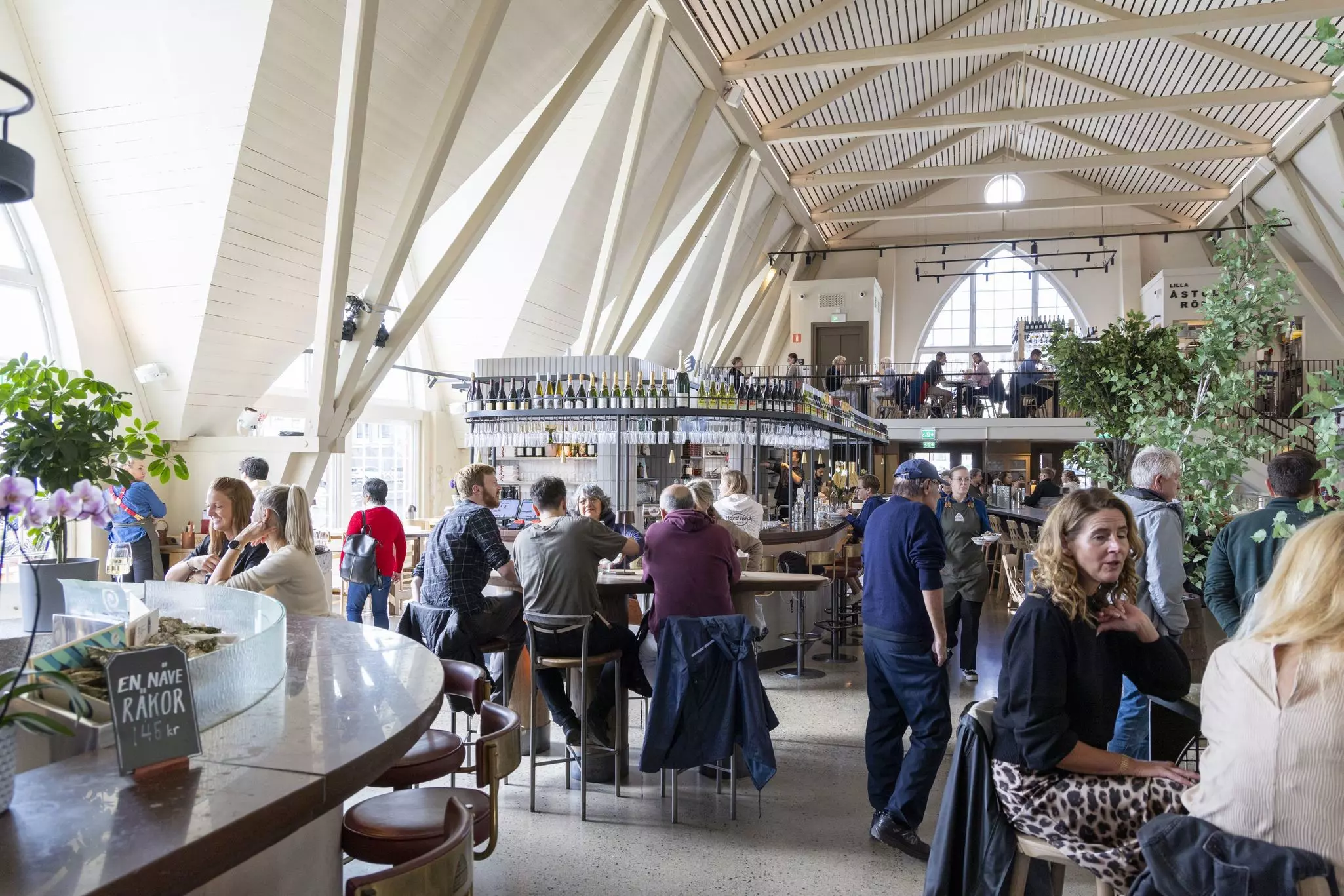 People sit at counters in a light-filled food hall with a high ceiling.