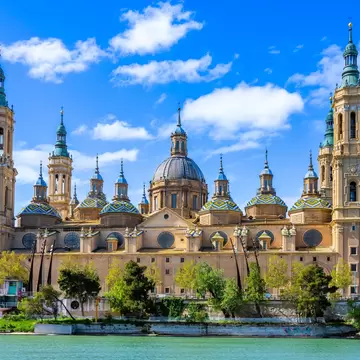 Basílica del Pilar in Zaragoza, Spain: four bell towers and green, yellow and blue tiled domes seen across the river