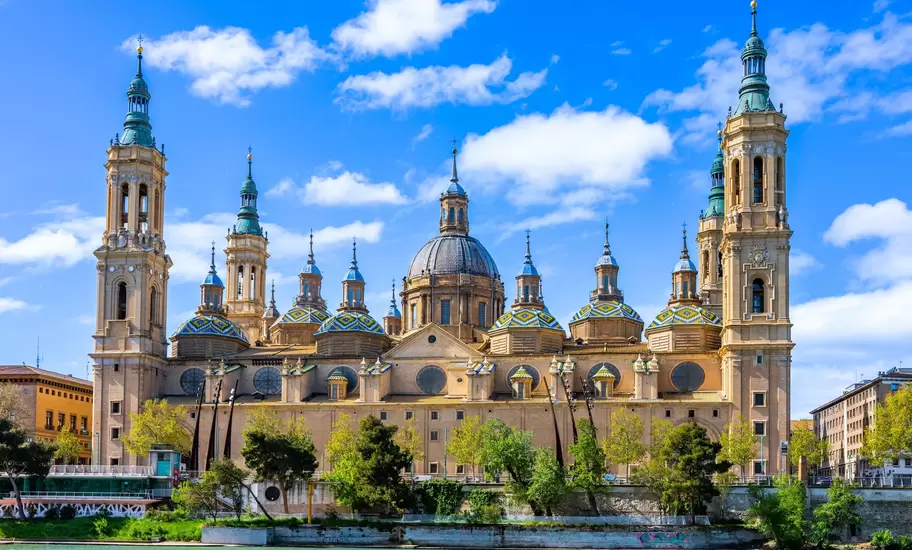 Basílica del Pilar in Zaragoza, Spain: four bell towers and green, yellow and blue tiled domes seen across the river