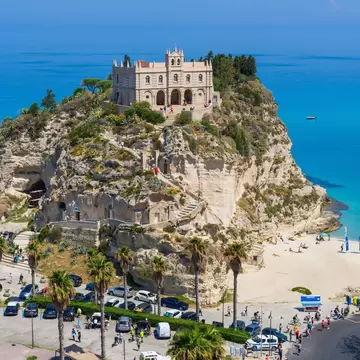 Steps weave a path around a cliff to a church. The cliff is surrounded by beautiful turquoise ocean with a sandy beach.