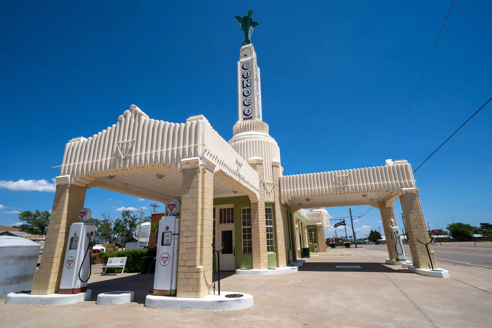A historic gas station with elaborate art deco architecture is pictured under a cloudless blue sky.