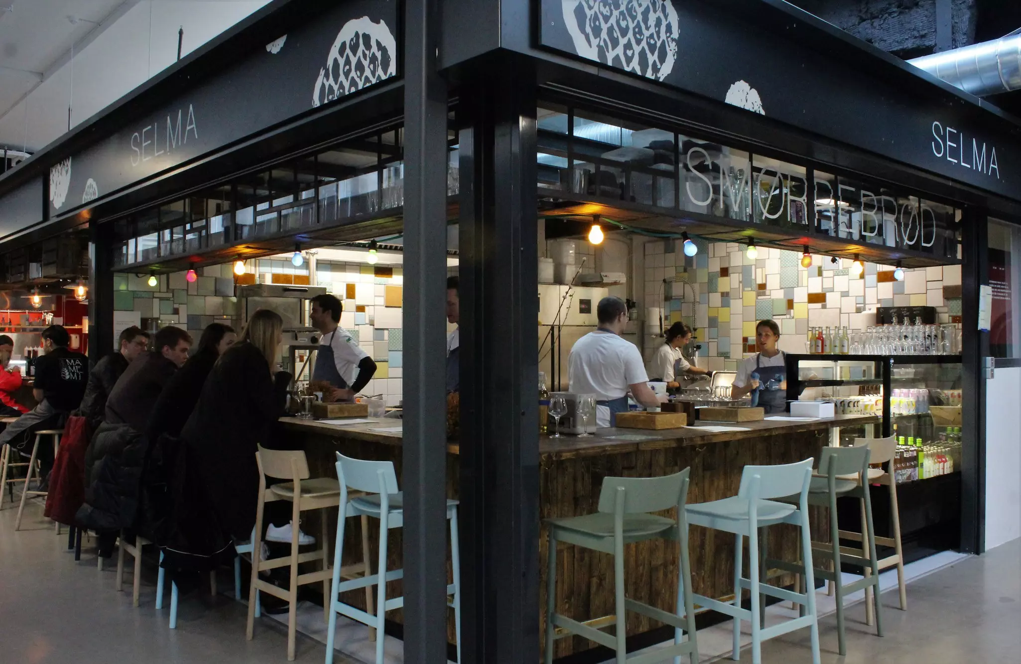 The interior of Selma restaurant in Copenhagen; it has floral wallpaper and wooden tables with mismatched chairs.