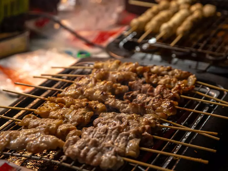 ."Grilled pork skewers" are cooked on a grill on th street. 