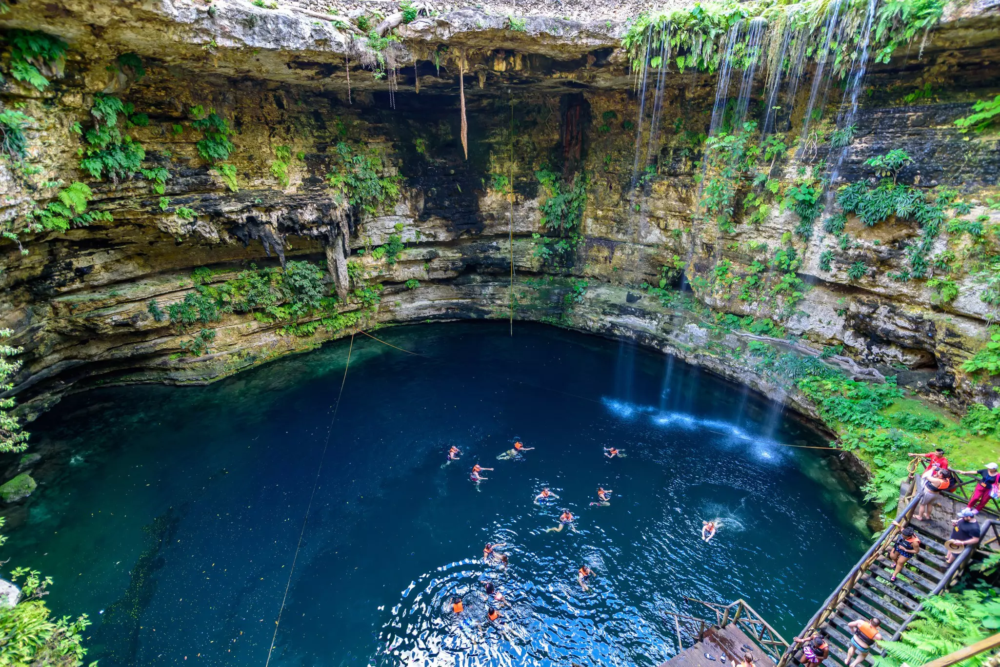 A view from above of people swimming in a pool at the bottom of a cavern.