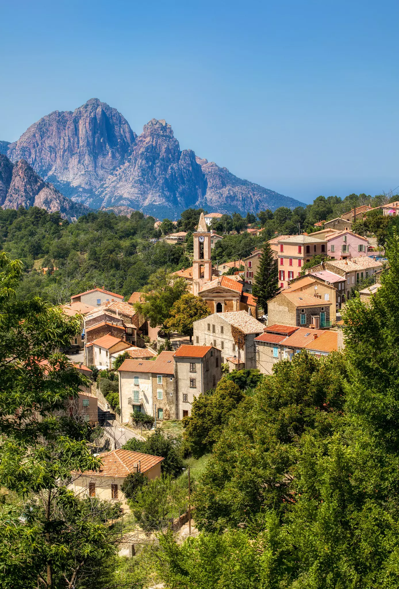 Mountains rise above a small village of red-roofed buildings.