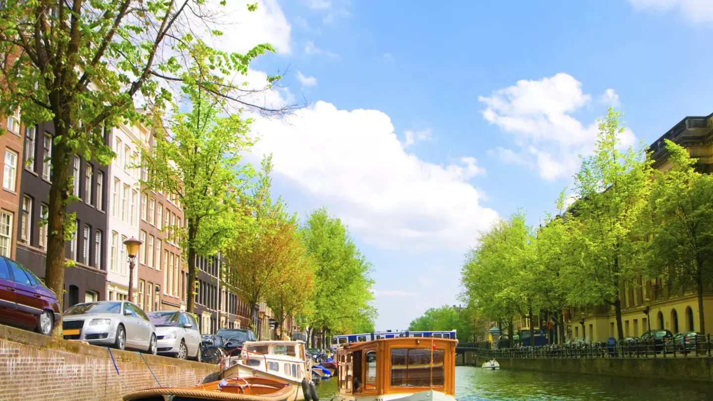 A blue-green canal in Amsterdam, with two small boats moored against a brick wall