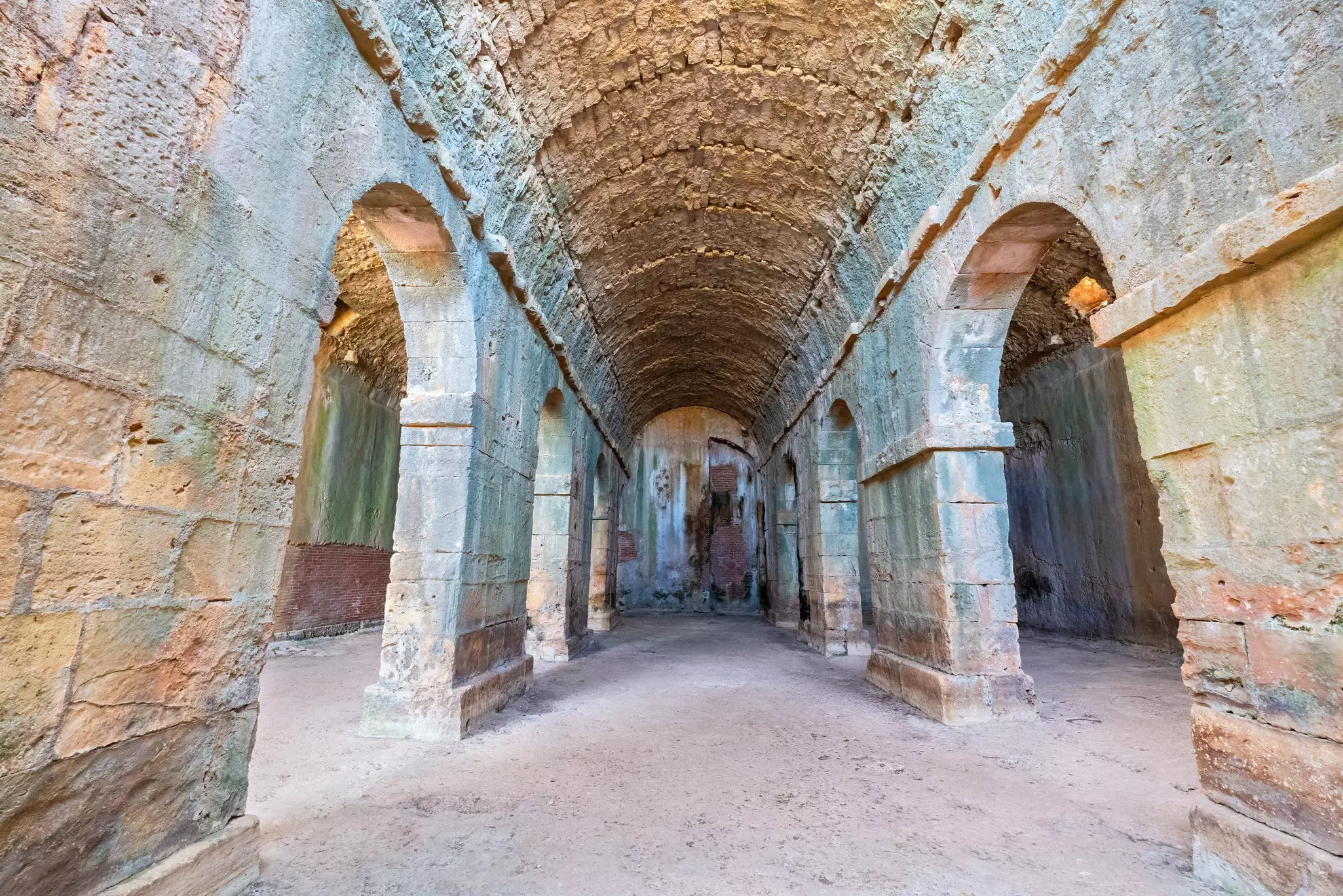 A wide view of a vaulted space with rounded arch opening on either side.