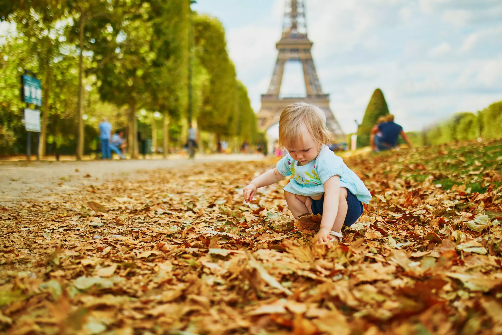 An adorable blond toddler girl plays with fallen autumn leaves near the Eiffel Tower in Paris, France