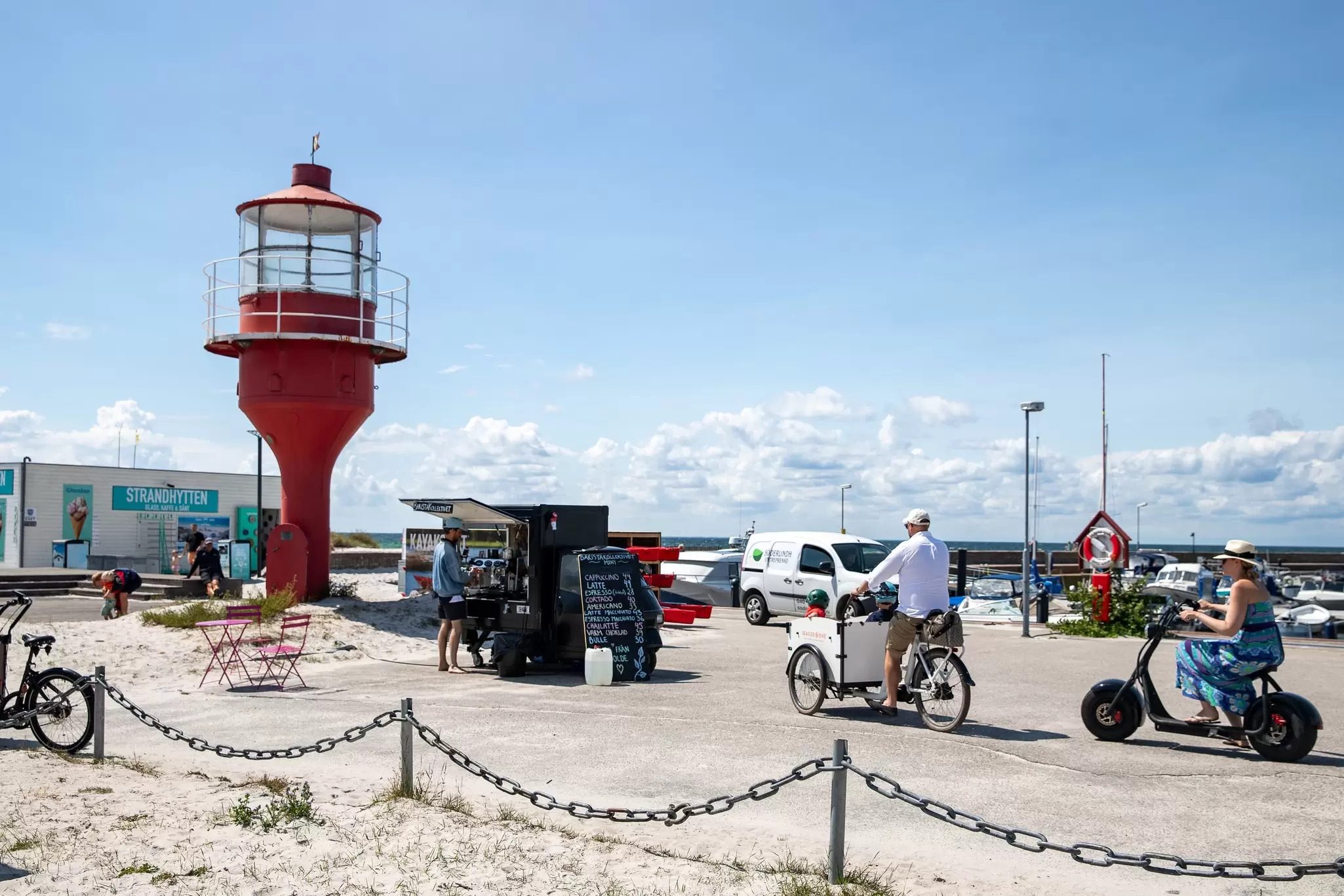 A cyclist and a coffee cart by a red lighthouse on a sunny day.