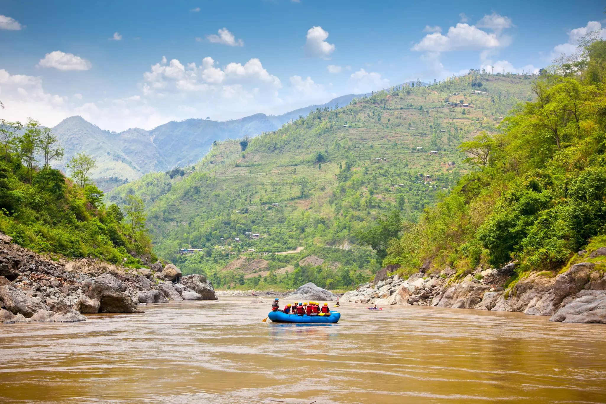 A raft loaded with people sets sail on a river with steep valley sides.