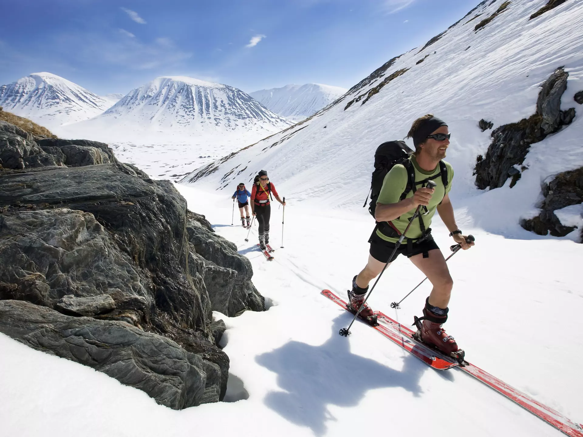 Three cross-country skiers move uphill as the sun shines down upon them