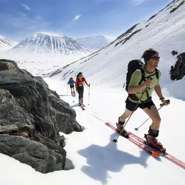 Three cross-country skiers move uphill as the sun shines down upon them