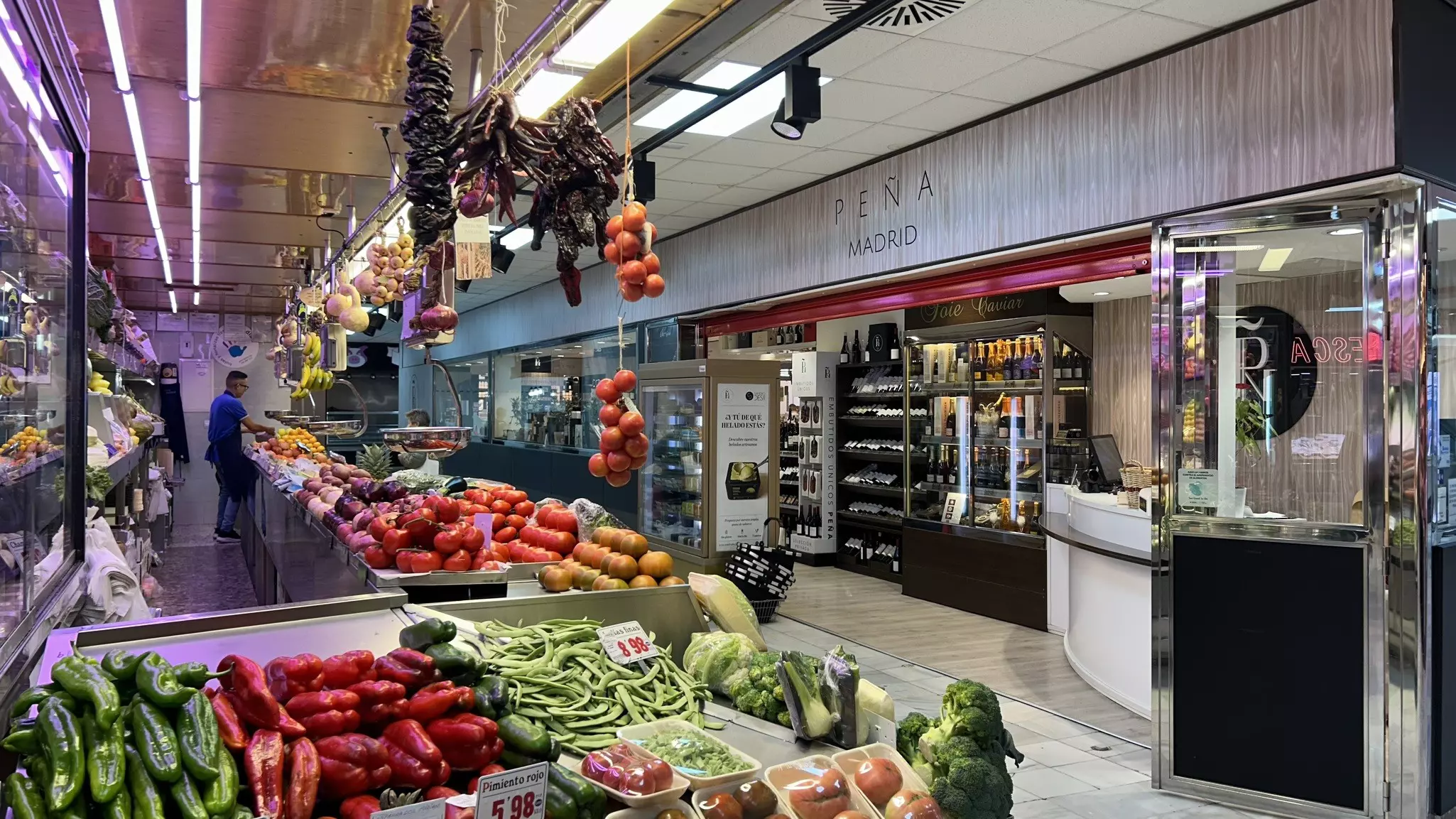A sleek indoor food market with colorful vegetables arranged in displays and hanging from the ceiling