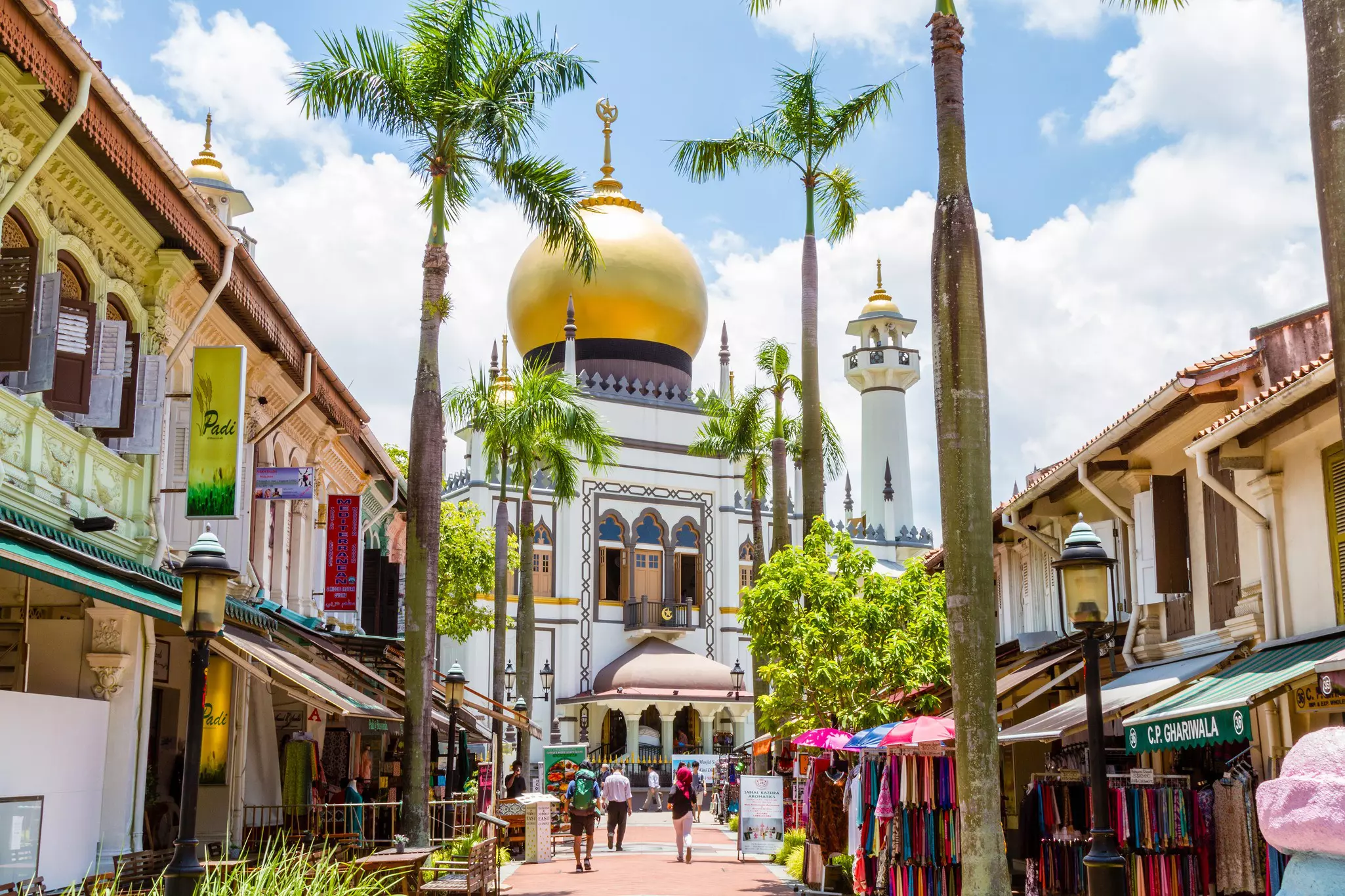 A path lined with palm trees leads to a golden domed mosque.