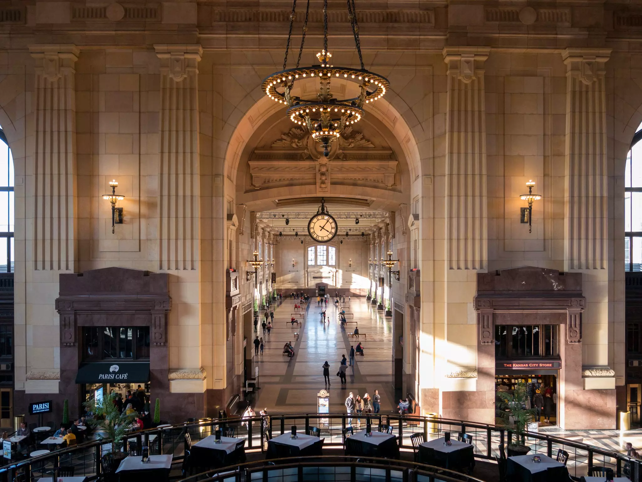 A vast concourse within a station with a huge clock and massive chandelier hanging down.