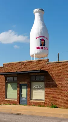 A giant milk bottle is displayed atop a small bright shop on a city street.