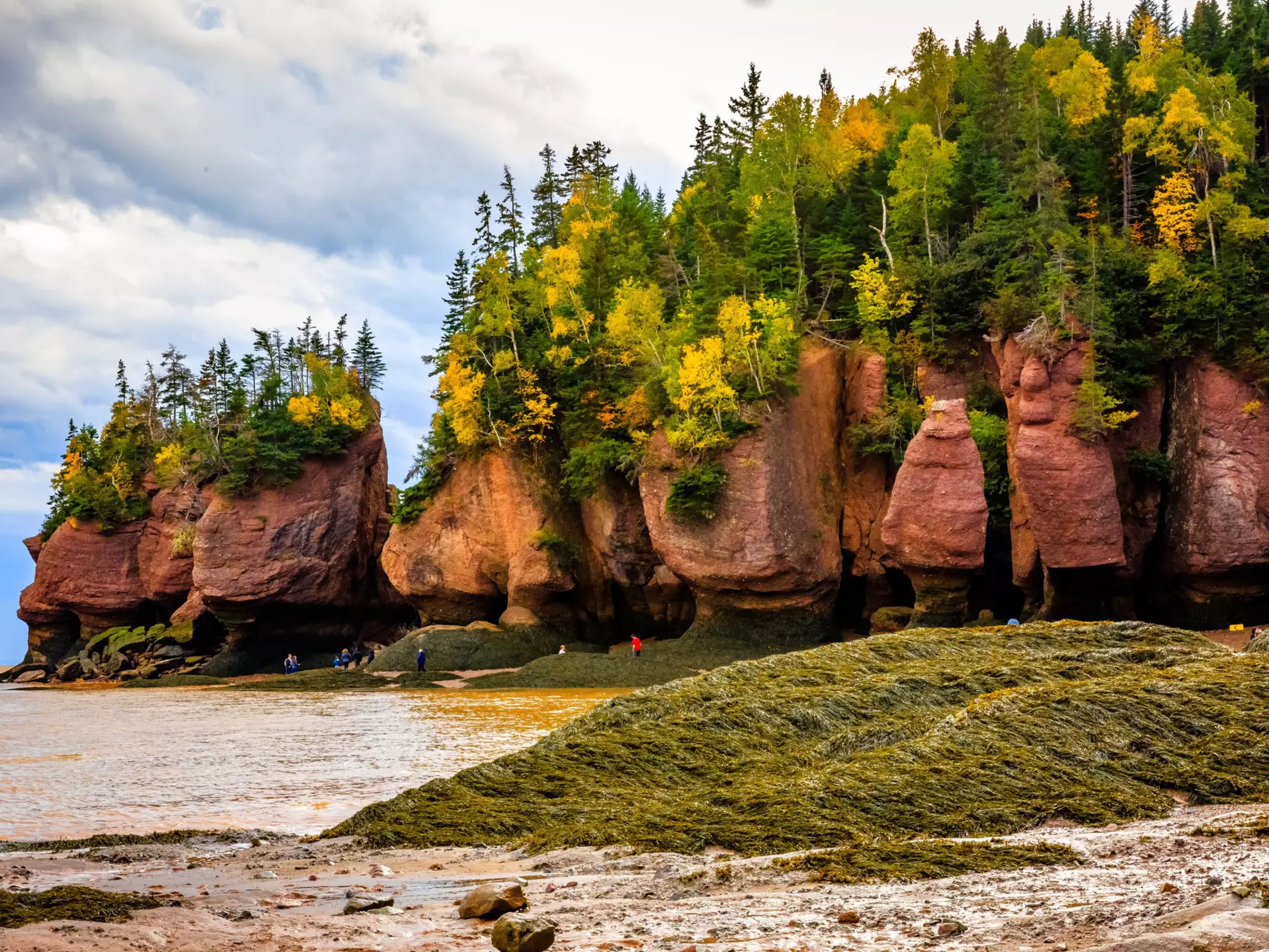 Visitors walk near large rock formations on the shore of a bay
