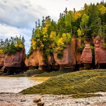 Visitors walk near large rock formations on the shore of a bay