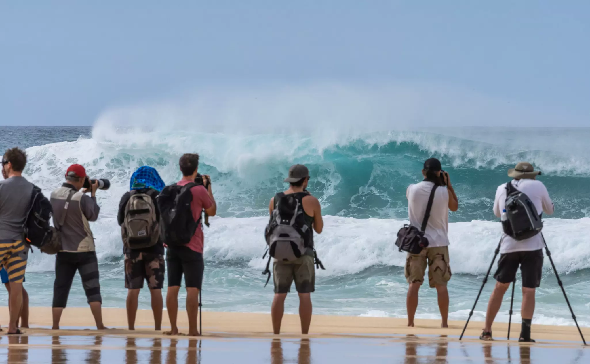 A group of spectators and photographers watches huge waves crash off shore at Pipeline, Oʻahu, USA