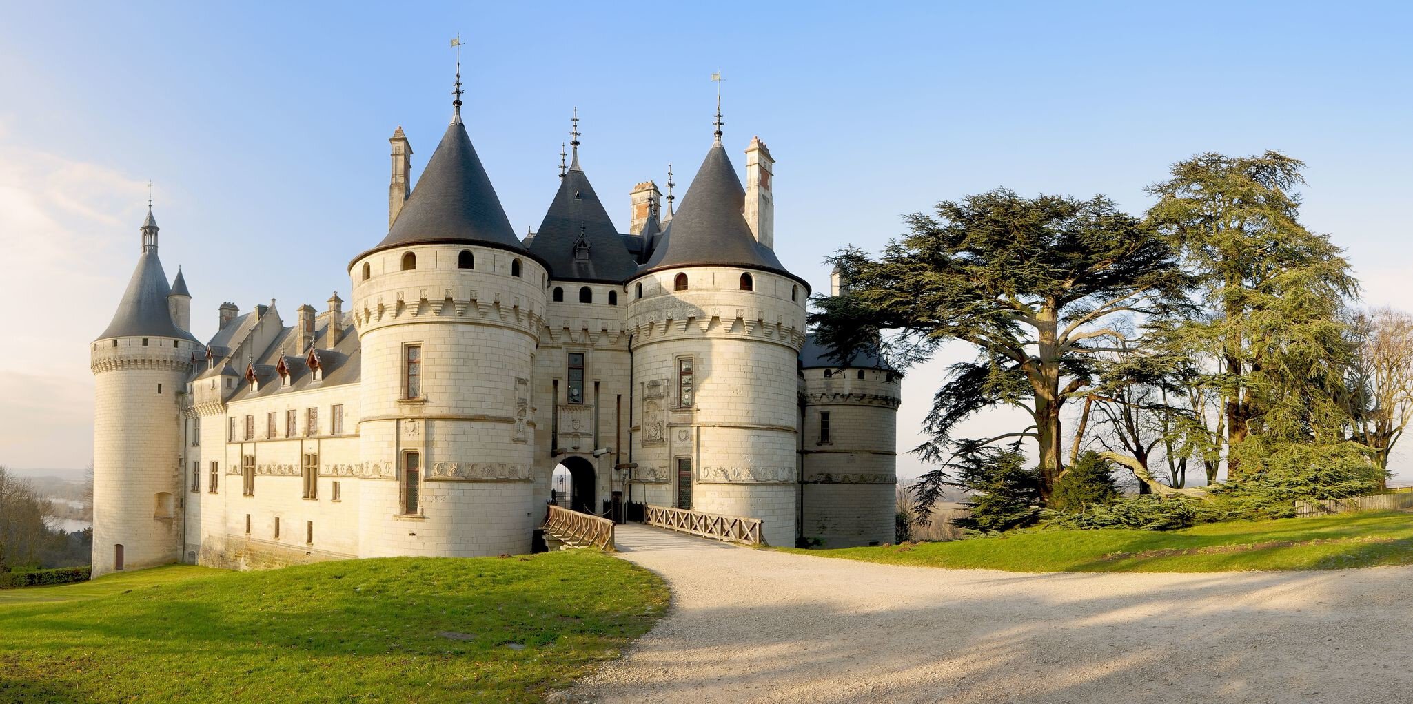 Chaumont Castle in Loire Valley France. Panoramic wide view to the entrance and the garden at sunrise with trees, grass under blue sky.
