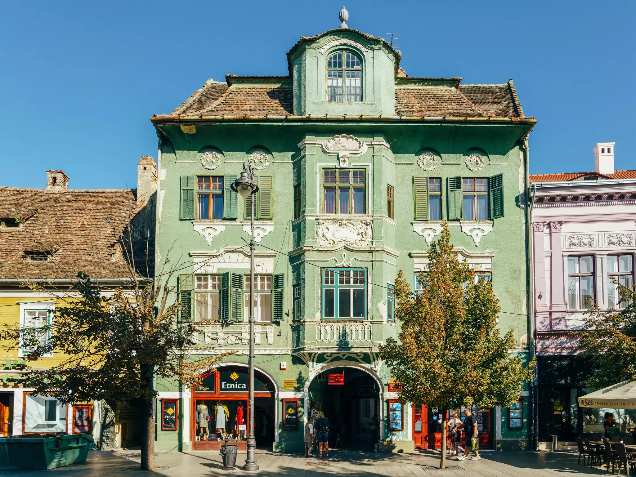 A green art deco-style building with wooden shutters and large windows. The ground floor is a store.