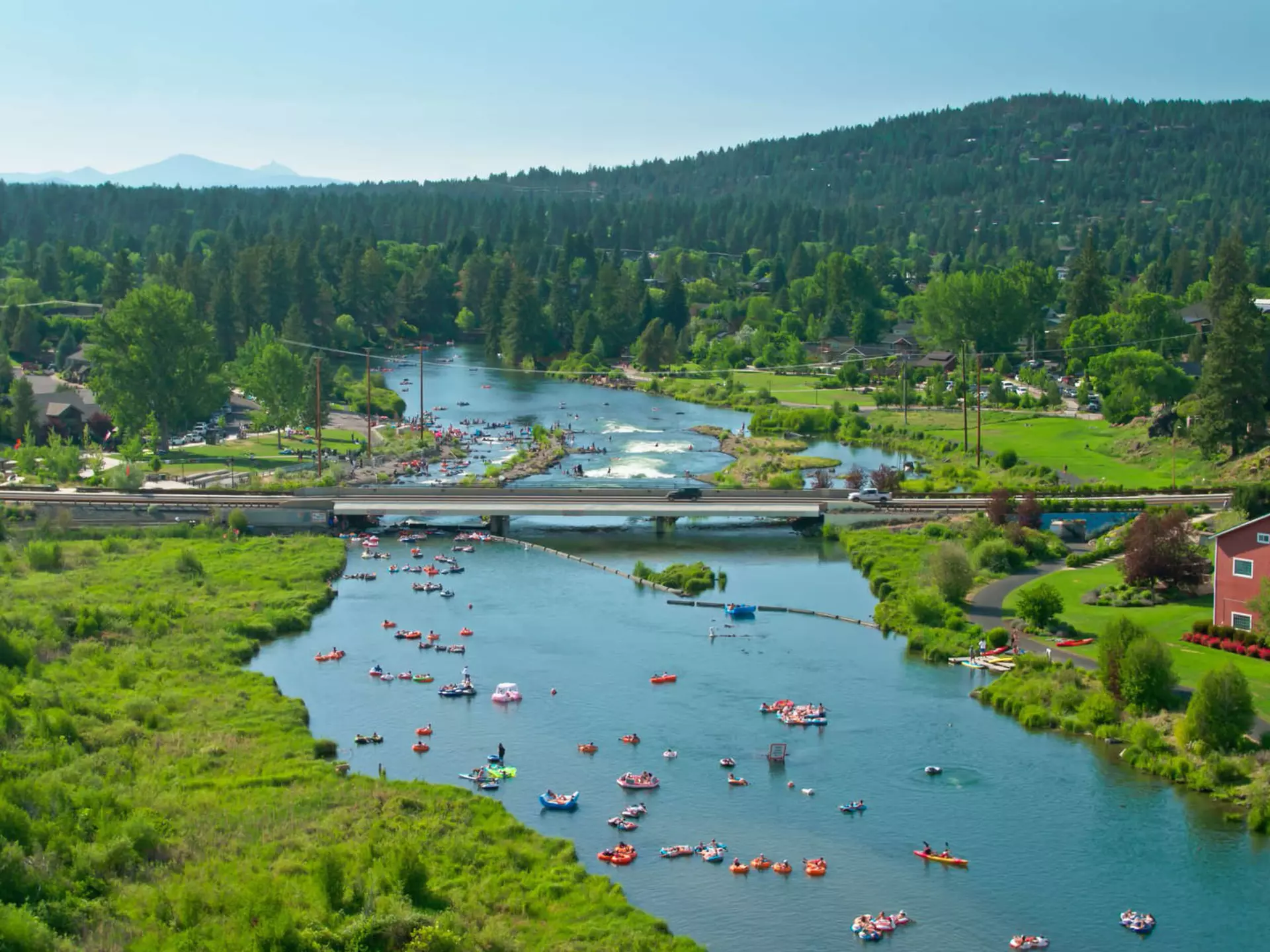 Two people are seen paddleboarding on a deep blue river from a vantage point far above on a rocky outcropping near Bend, Oregon