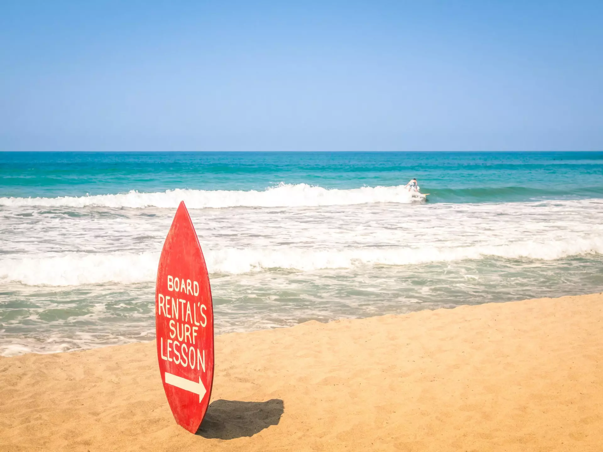 Surfboard rental and surf lesson sign on a sandy beach