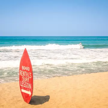 Surfboard rental and surf lesson sign on a sandy beach