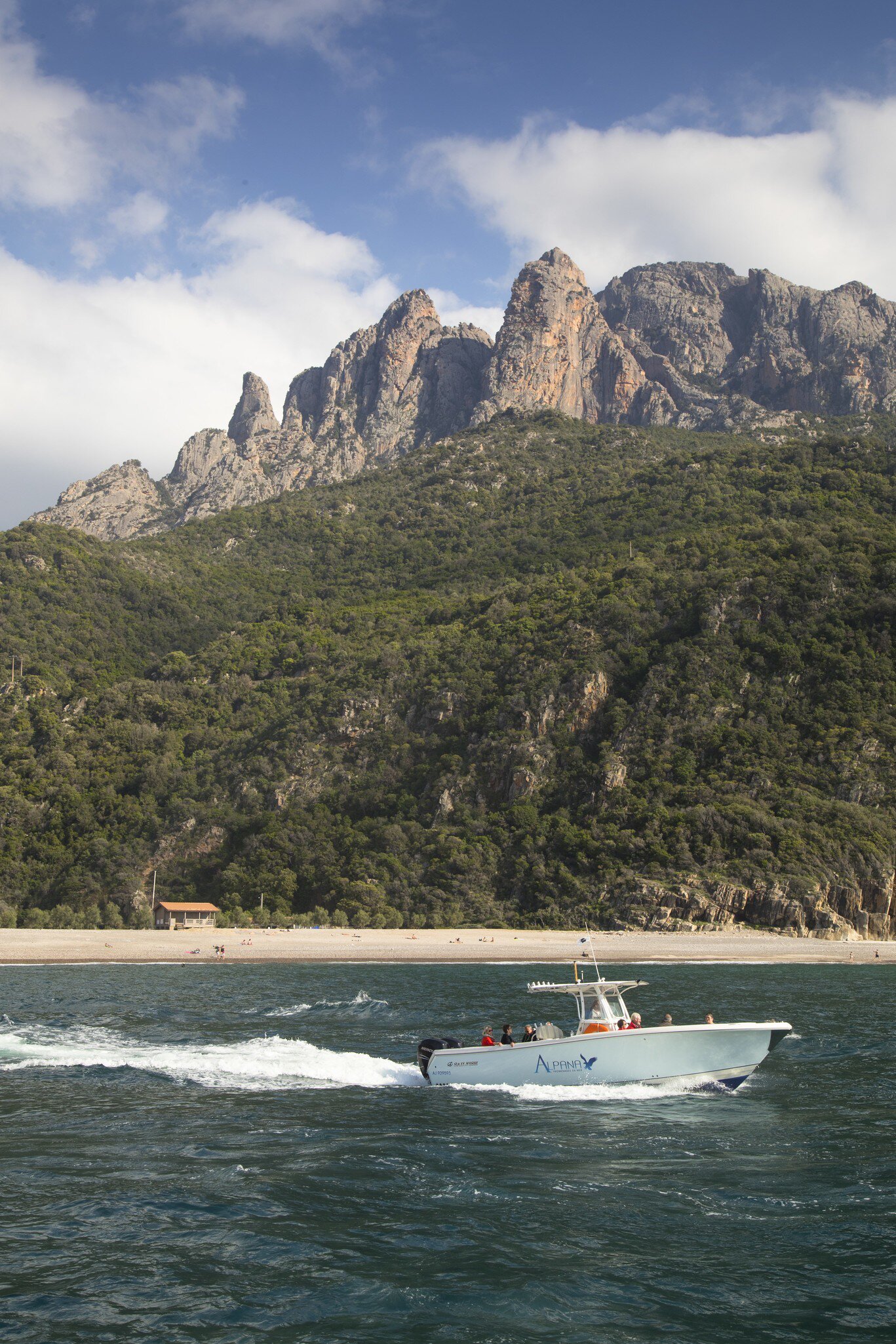 A motorboat passes a beach with the rocky cliff face of the Scandola Nature Reserve beyond. Corsica, France.