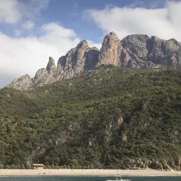 A motorboat passes a beach with the rocky cliff face of the Scandola Nature Reserve beyond. Corsica, France.
