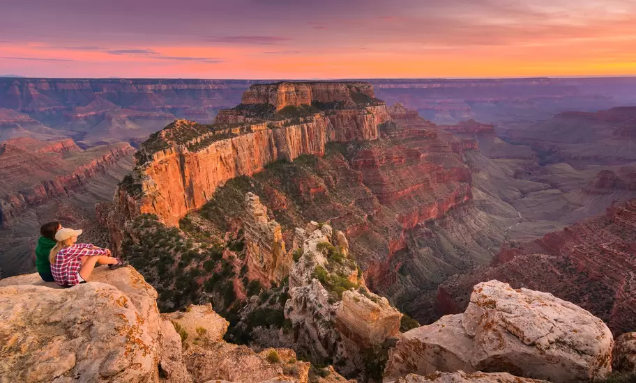 Group of people sitting near the edge watching sunset at Grand Canyon National Park North Rim, USA.