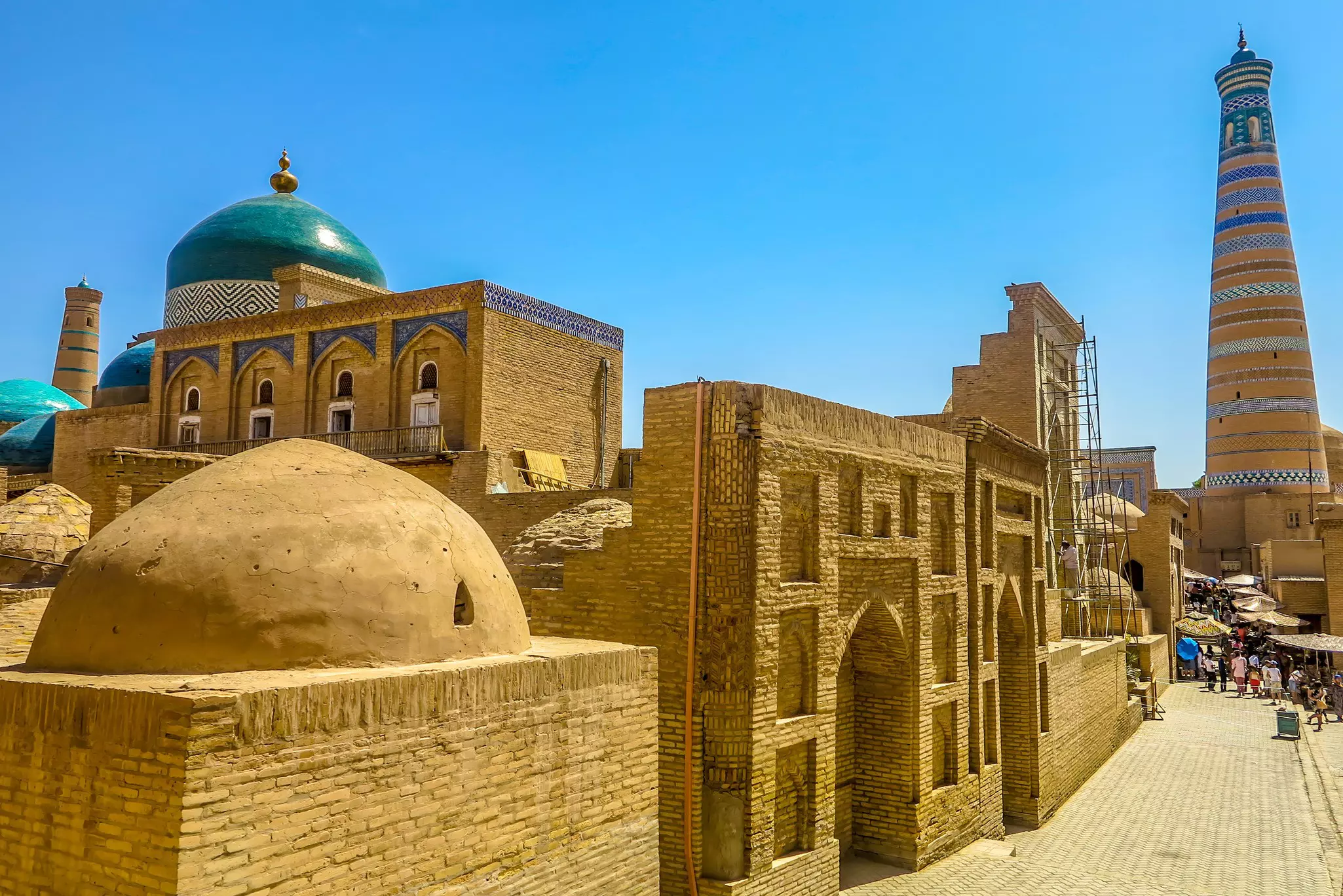 Mud brick structures with blue domes and visitors walking the streets