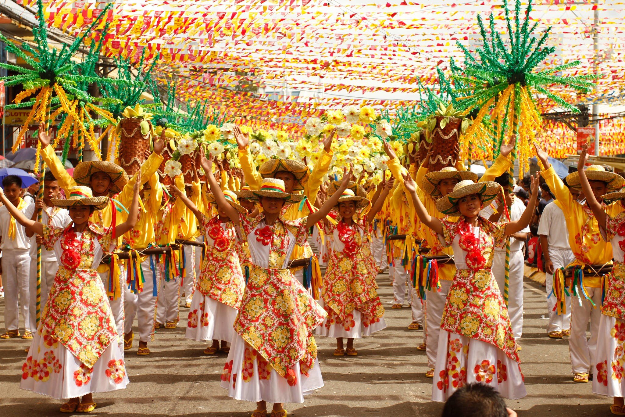 Rows of dancers in red and yellow floral dresses raise their arms beneath strings of festival bunting on a Cebu City street.