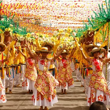 Rows of dancers in red and yellow floral dresses raise their arms beneath strings of festival bunting on a Cebu City street.